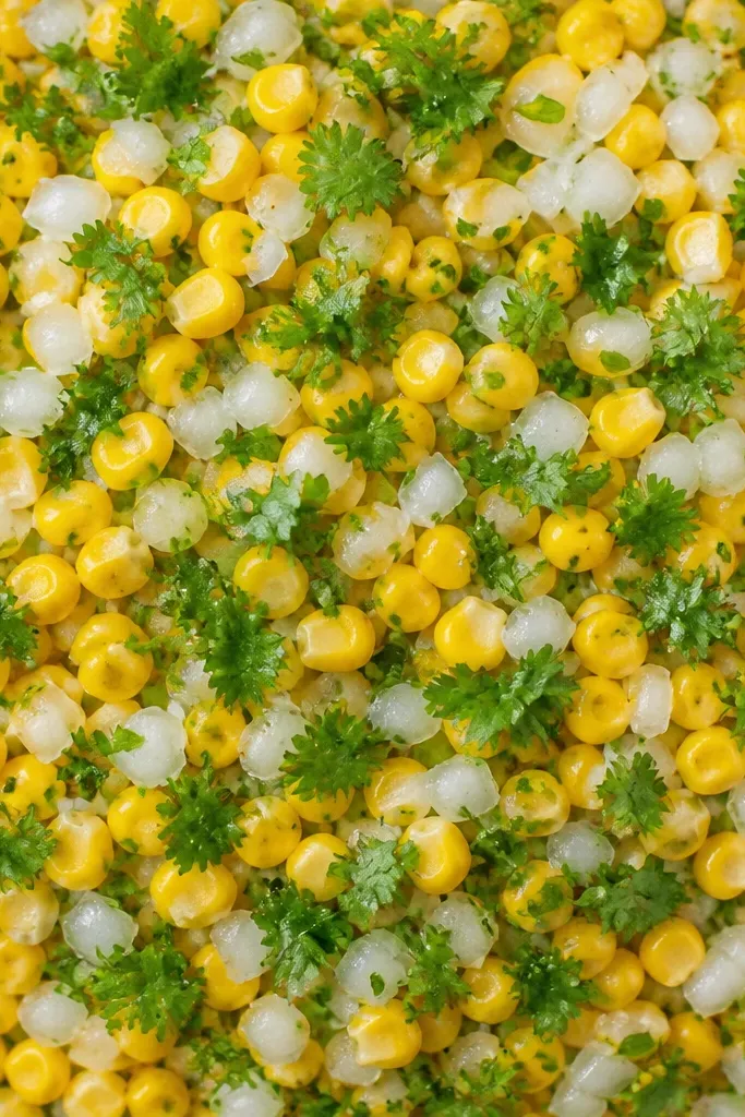 Top-down view with bright green cilantro sprinkled evenly, not clumped, over a corn and onion base.