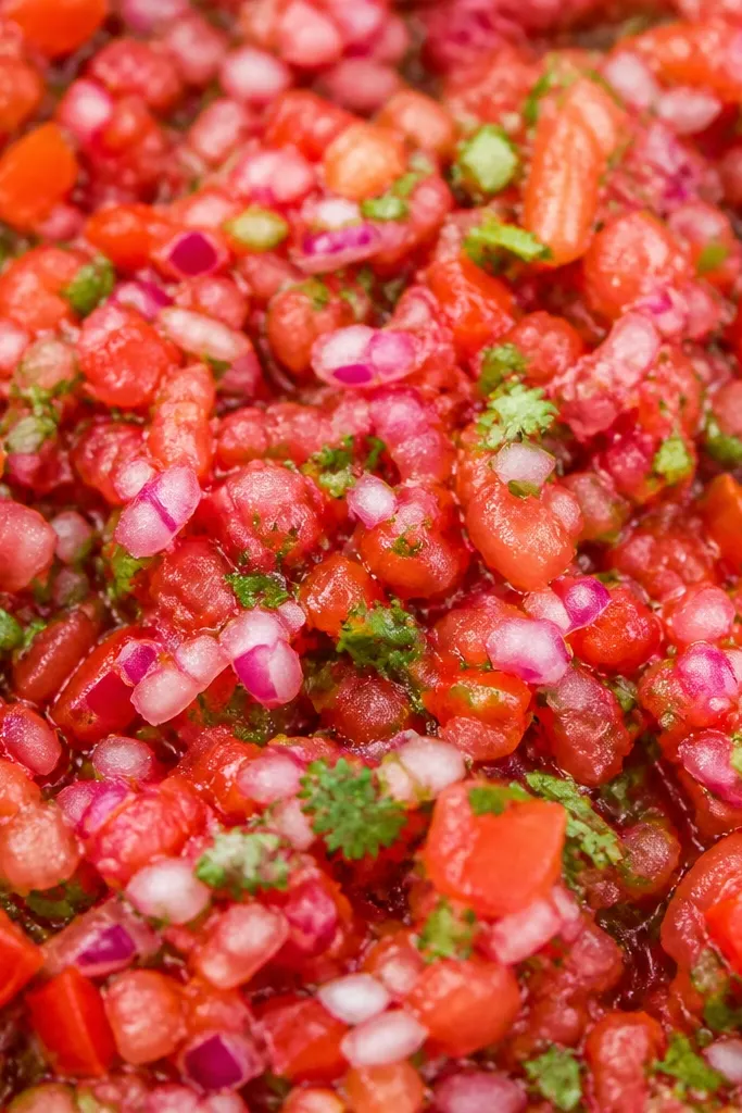 Close-up of salsa showing red onion bits that look pinkish in some spots and purple in others. The onion is finely chopped and evenly spread, with no big chunks.