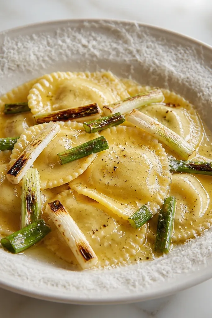 Ravioli arranged with charred spring onion segments on top. The sauce is mostly butter with a light sheen. A thin border of parmesan is grated around the rim of the plate.
