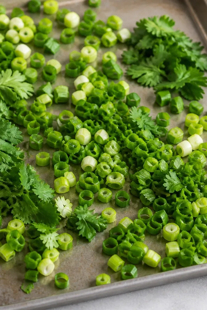 A tray where chopped scallions and cilantro leaves are scattered across the top in uneven piles. The greens look fresh, not wilted, with bright light-green stems and dark-green leaves.